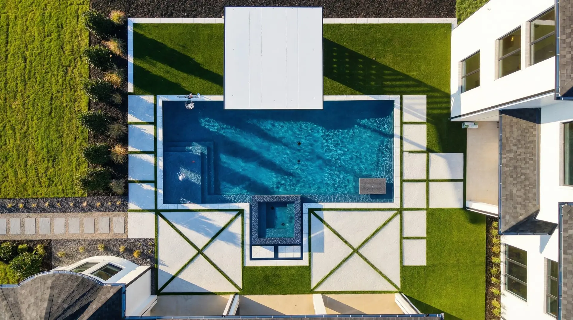 Overhead view of a geometric pool with a raised spa, turf-inlay decking, and a pergola beside the home in a Celina, TX backyard built by Prestige Pool & Patio