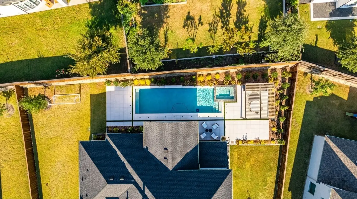 Aerial view of a long rectangular pool with a spa and pergola set in a wide lawn in a Prosper, TX backyard built by Prestige Pool & Patio